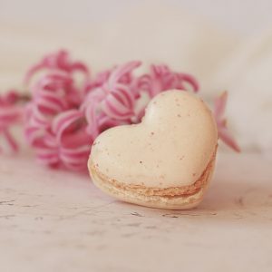 Macaroon shaped like a heart and pink flowers in the background
