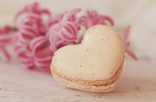 Macaroon shaped like a heart and pink flowers in the background
